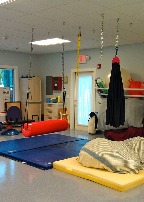 A bolster swing for physical therapy hangs from the ceiling in a room of PT equipment.